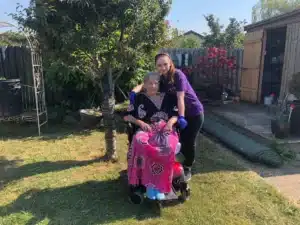 A Pride Homecare staff member providing support to an elderly lady in a wheelchair, enjoying the tranquility of a well-tended garden, demonstrating the compassionate care they offer